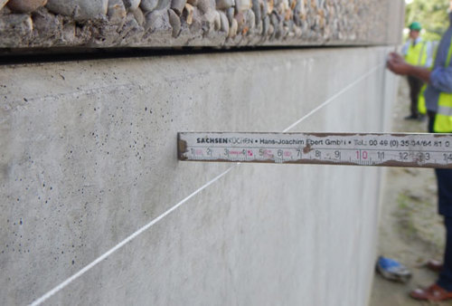 De kromming van een betonnen element wordt gemeten met behulp van een opgespannen touw en een vouwmeter.